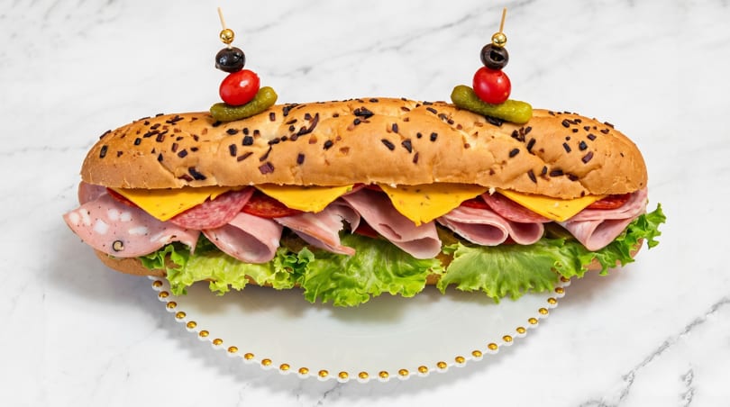 A large submarine sandwich filled with various meats, cheese, and lettuce on a white plate.