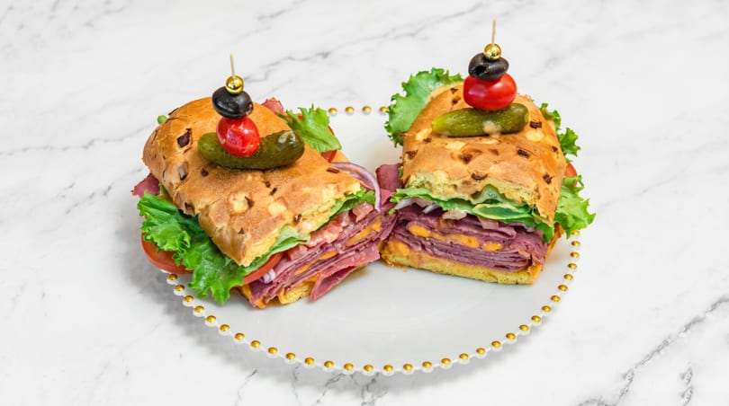 Two halves of a deli sandwich with meat, cheese, lettuce, and tomato on a white plate.