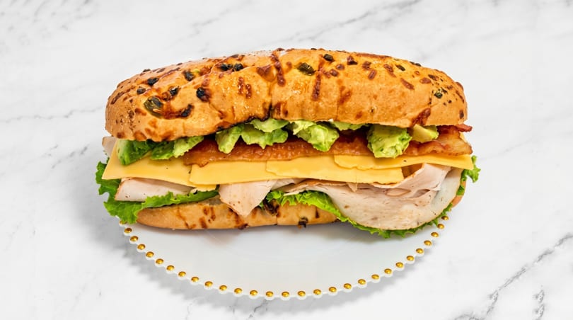 A large turkey, bacon, avocado, and cheese sandwich on a jalapeño cheddar roll.